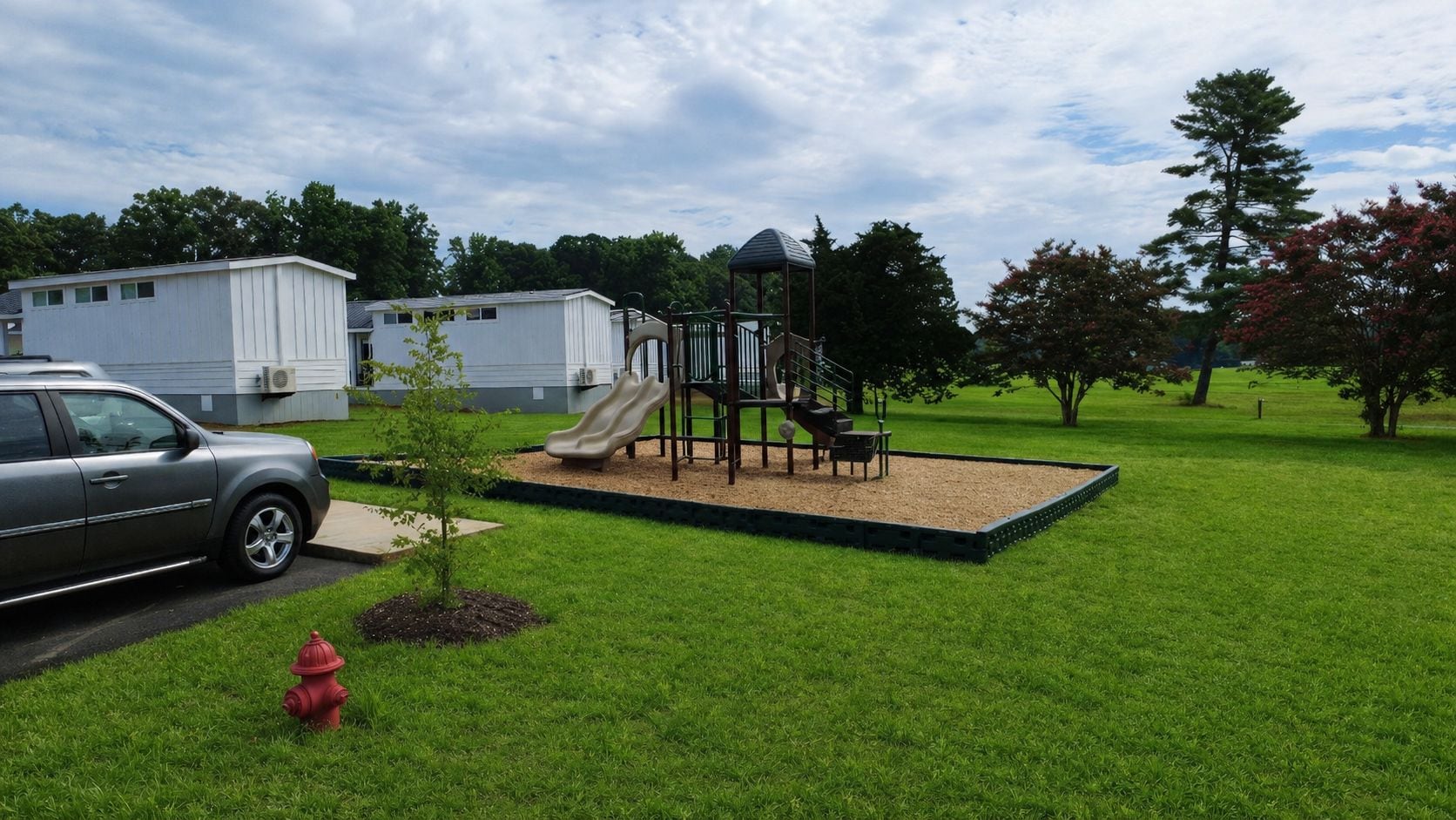 Un parque infantil con tobogán y estructura para escalar, rodeado de césped y árboles.