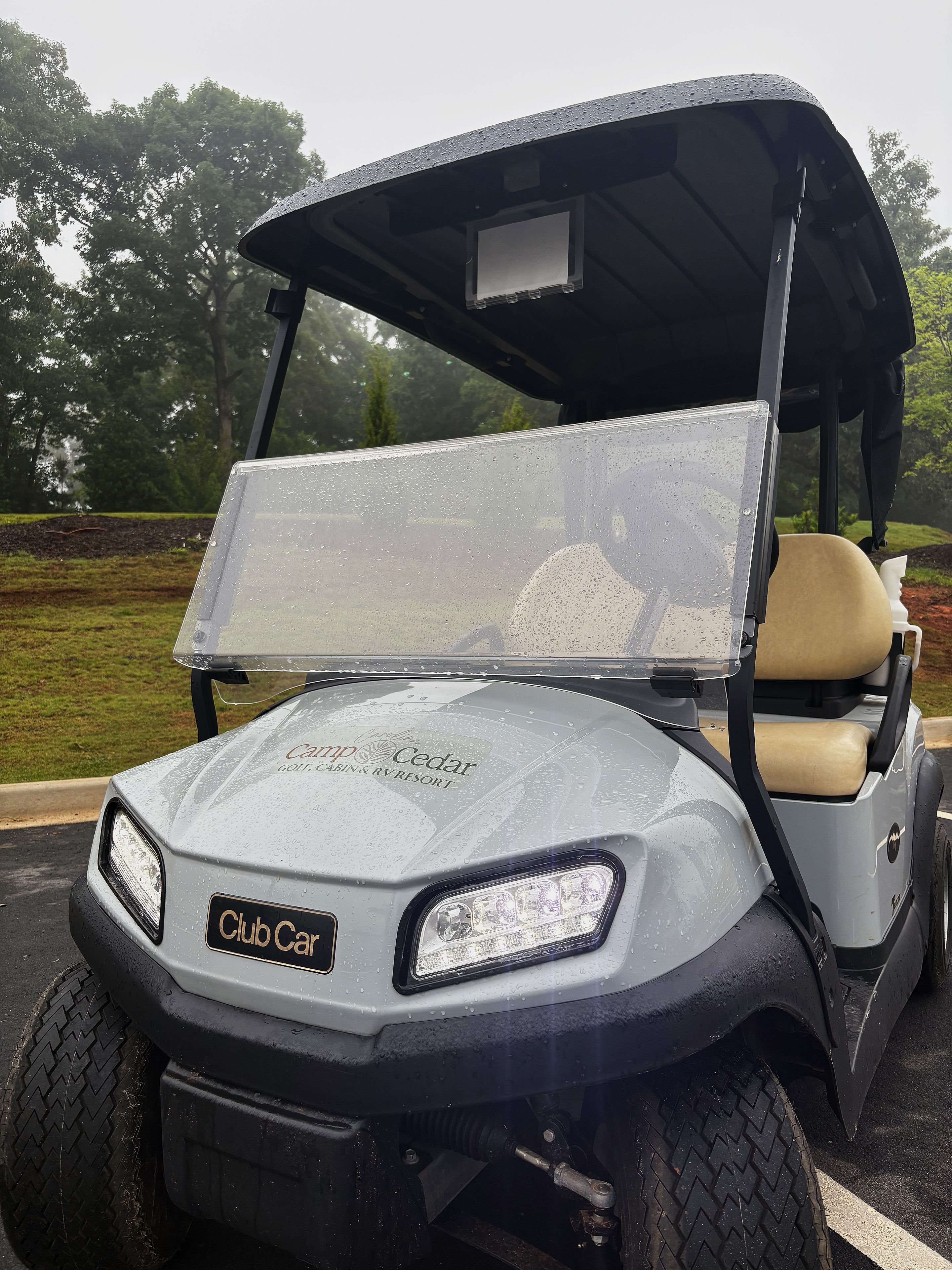 Une voiturette de golf Club Car dotée d’un pare-brise transparent, d’un siège visible et d’un logo à l’avant.