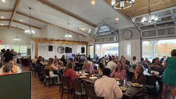 A spacious dining area with wooden beams and chandeliers, featuring multiple tables and chairs.