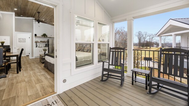 A spacious porch with wooden flooring, a dining area with a table and chairs, and a view of the surrounding landscape. - Carolina Camp Cedar (Pickens)