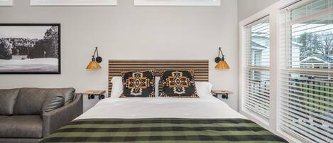 Ein Schlafzimmer mit einem großen Bett, zwei Nachttischen, einem hölzernen Kopfteil und einem Fenster mit Jalousien.