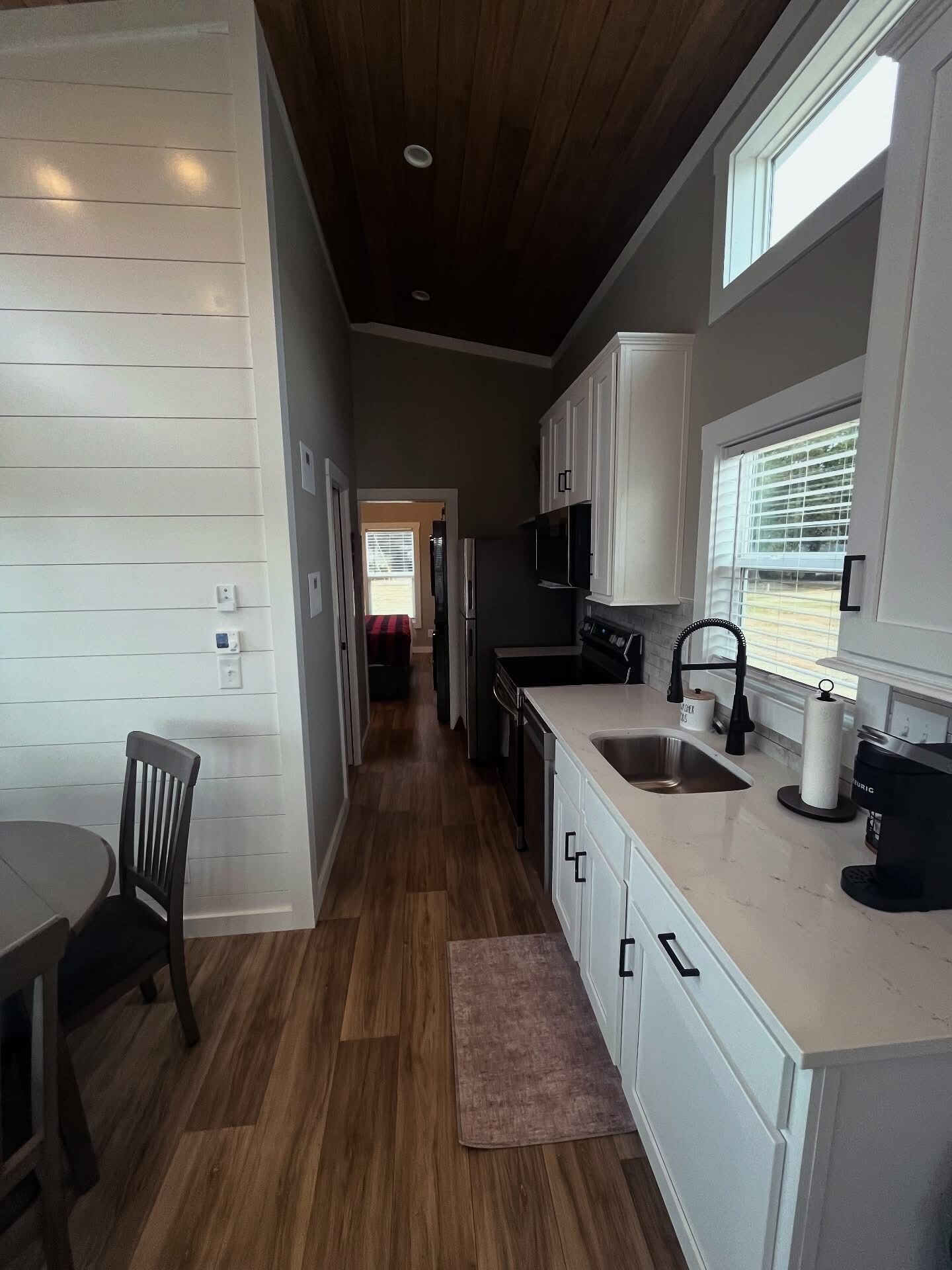 A modern kitchen with white cabinetry, a wooden floor, and a view of the backyard through a window.