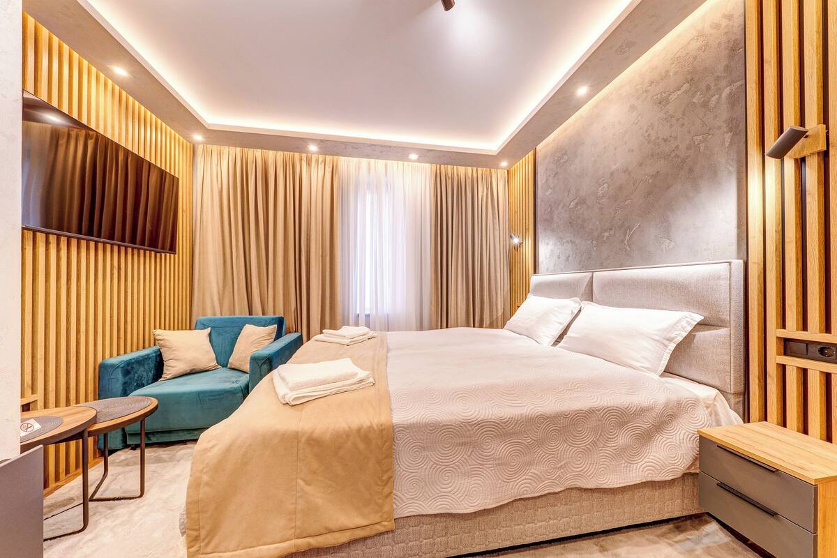 Una habitación de hotel moderna con una cama grande, un sofá, un escritorio y un televisor montado en la pared.