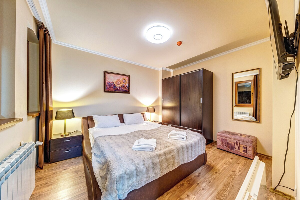 Ein Schlafzimmer mit einem Bett, Nachttischlampen, einem Kleiderschrank, einer Heizung und einem an der Wand montierten Fernseher.