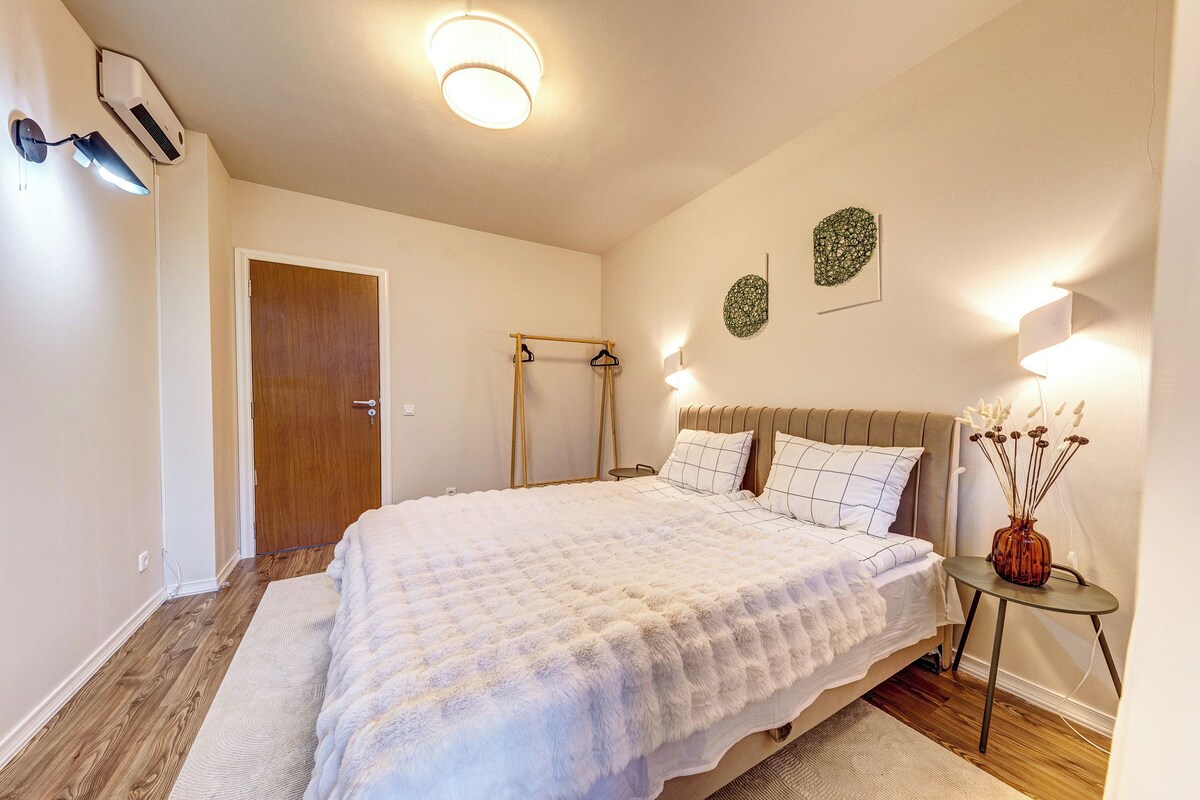 Een slaapkamer met een bed, nachtkastje, wandairconditioner en een deur.