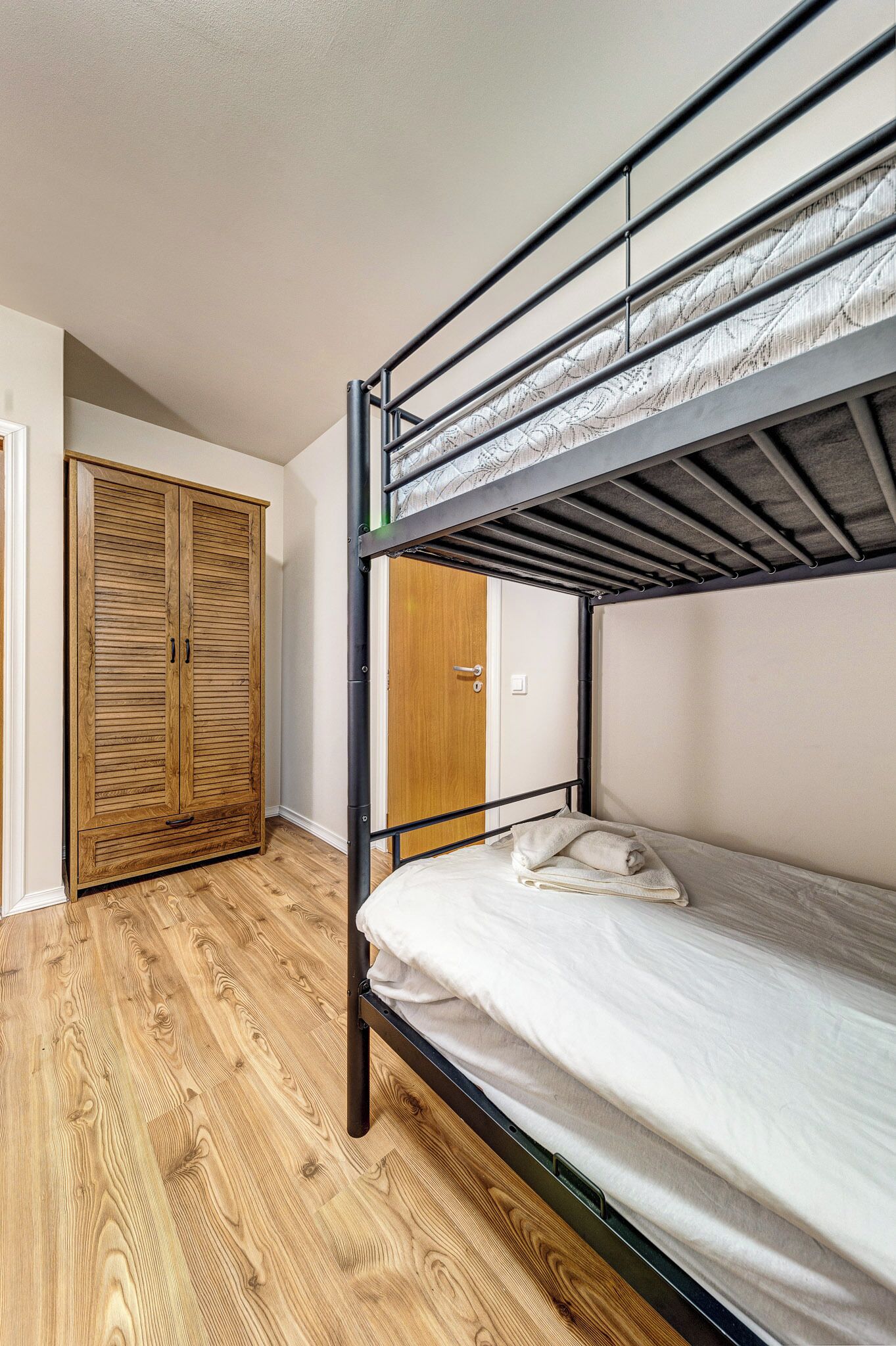 Un lit superposé avec une armoire en bois et une porte dans une pièce dont le sol est recouvert de planches de bois.