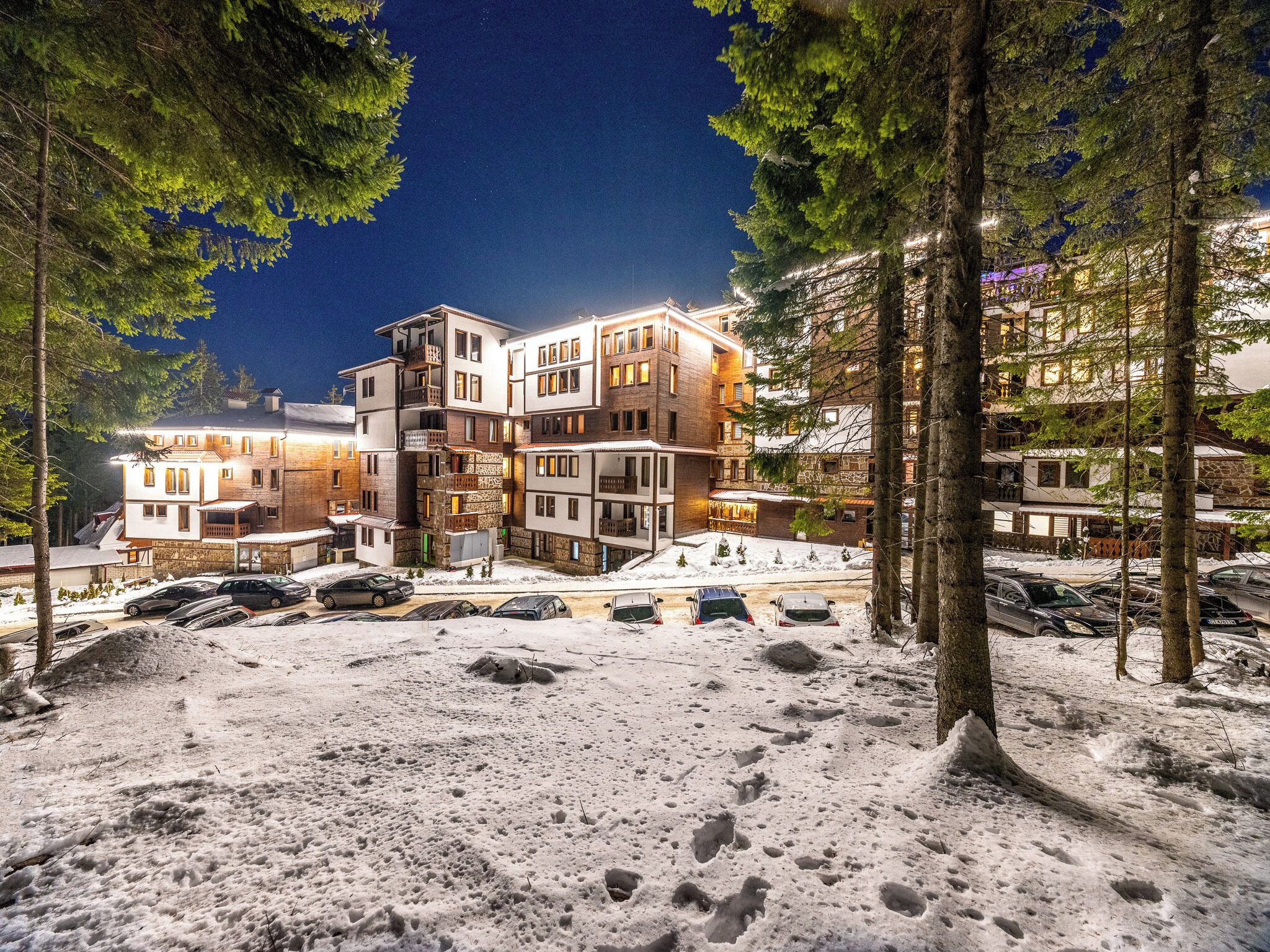Un hotel de varios pisos con diseño moderno, que cuenta con balcones y un estacionamiento con varios coches.