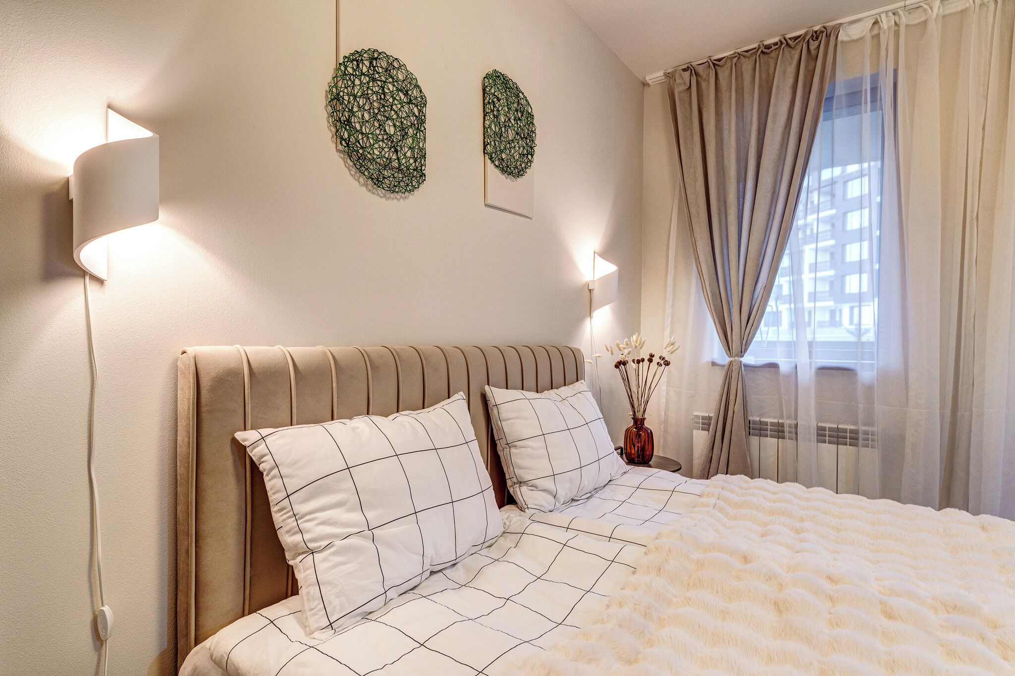 A neatly made bed with a white and black checkered bedspread, a beige headboard, and two pillows with a similar pattern.