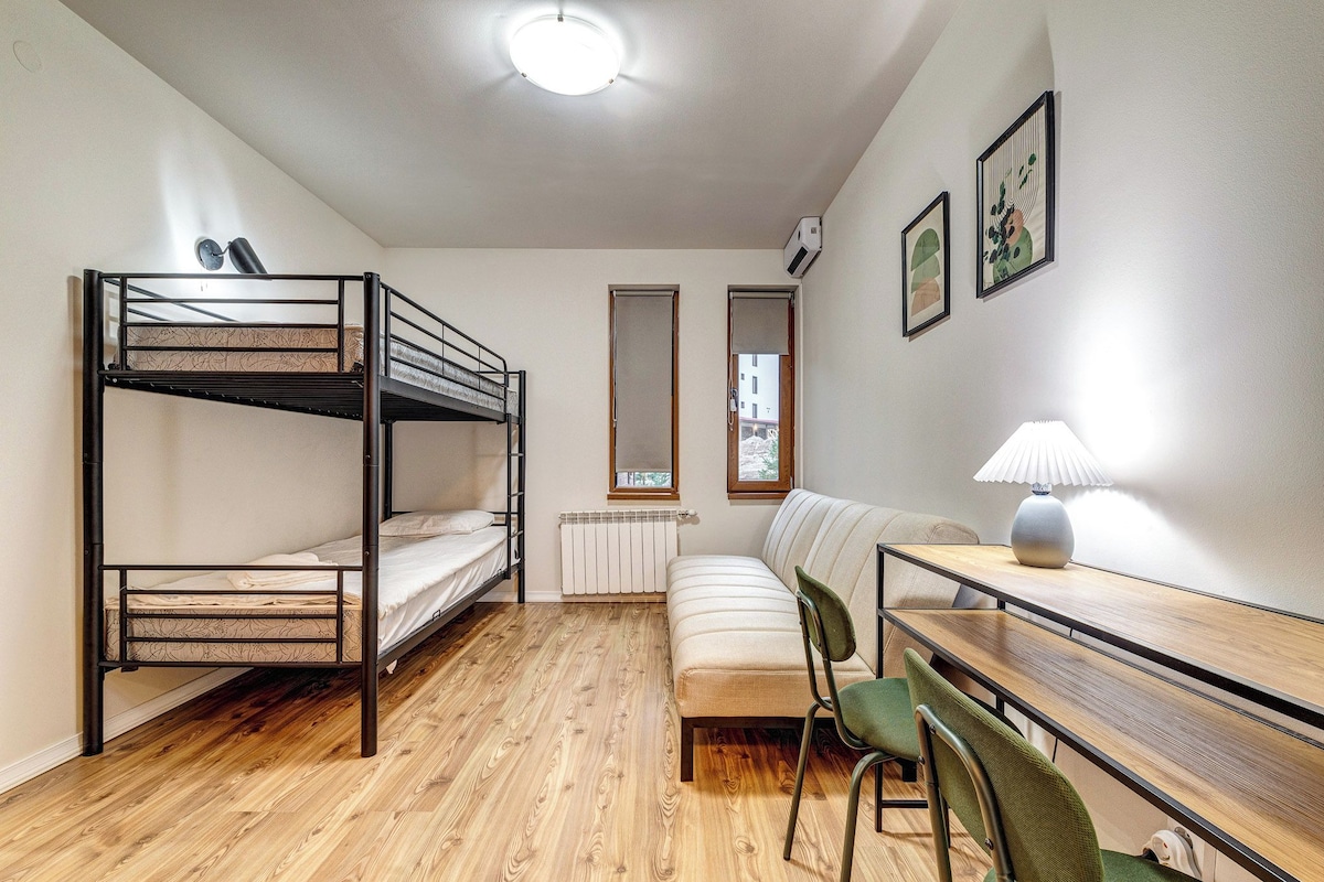 Ein Schlafsaalzimmer mit Etagenbetten, einer Schlafcouch, einem Tisch mit Lampe und einem Heizkörper.