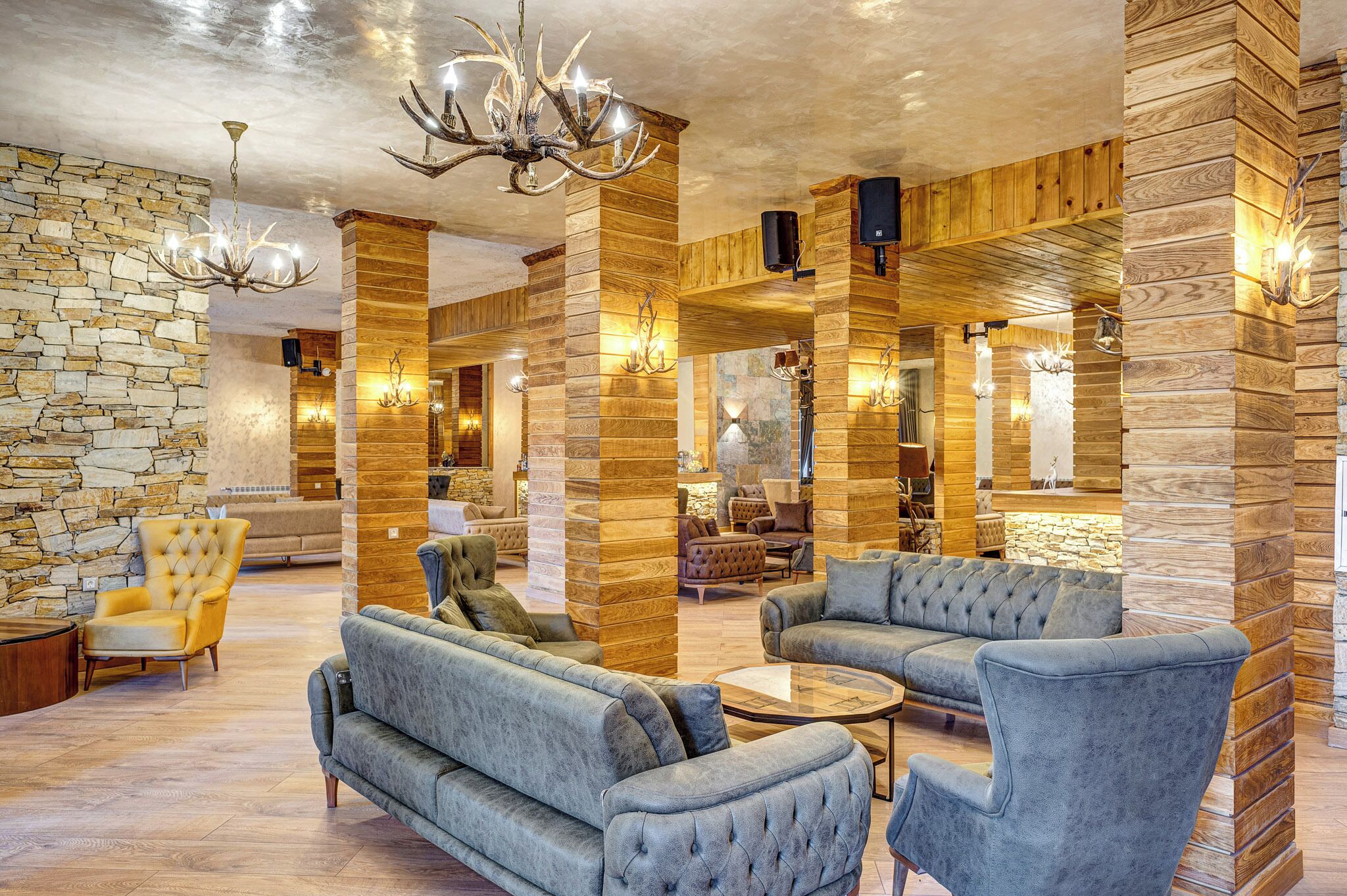 Un hall d’entrée spacieux avec un mur en pierre, des lambris en bois et un lustre. On y trouve des canapés et des fauteuils confortables, ainsi qu’une table basse.
