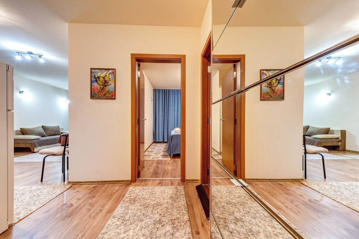 Ein Korridor mit Holzboden, einer zentralen Tür, die zu einem Schlafzimmer führt, und zwei Sofas auf jeder Seite.