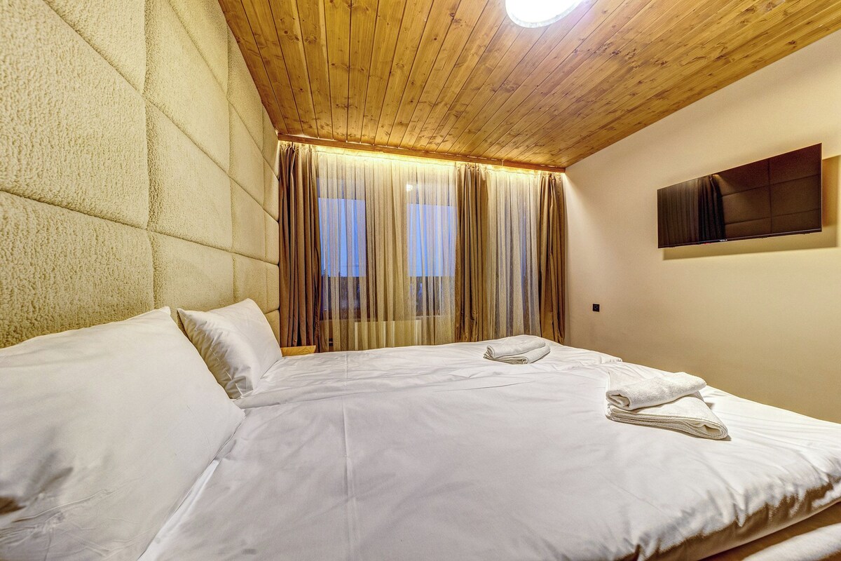 Une chambre d’hôtel avec un grand lit, un plafond en bois et un téléviseur à écran plat fixé au mur.