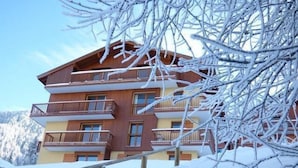 A multi-story wooden building with balconies, surrounded by snow-covered trees and mountains. - 100m from ski slopes, 3rd floor, balcony, ski locker, 90m², Valfréjus (Valfréjus)