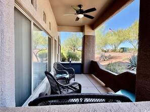 A balcony with wicker furniture, a ceiling fan, and a view of desert vegetation.