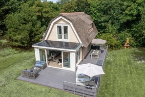 A modern house with a large glass door leading to an open patio area with outdoor furniture. - Charming Country House for 4 People (De Koog)