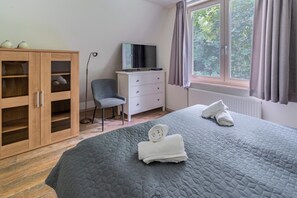 A bedroom with a bed, a wardrobe, a chair, a TV, and a window with curtains. - Charming Country House for 4 People (De Koog)