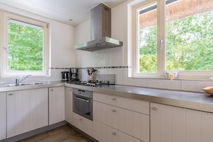 Una cocina moderna con armarios blancos, electrodomésticos de acero inoxidable y grandes ventanales con vistas a zonas verdes.