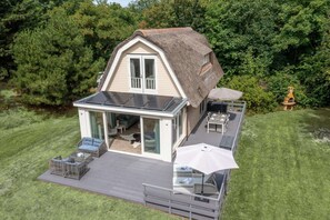 A modern house with a thatched roof, a glass door entrance, and a patio area with outdoor furniture. - Charming Country House for 4 People (De Koog)