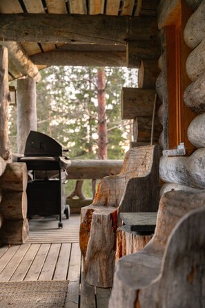 Ein rustikales Blockhaus im Inneren, mit Holzbänken und einem Grill vor der Tür.