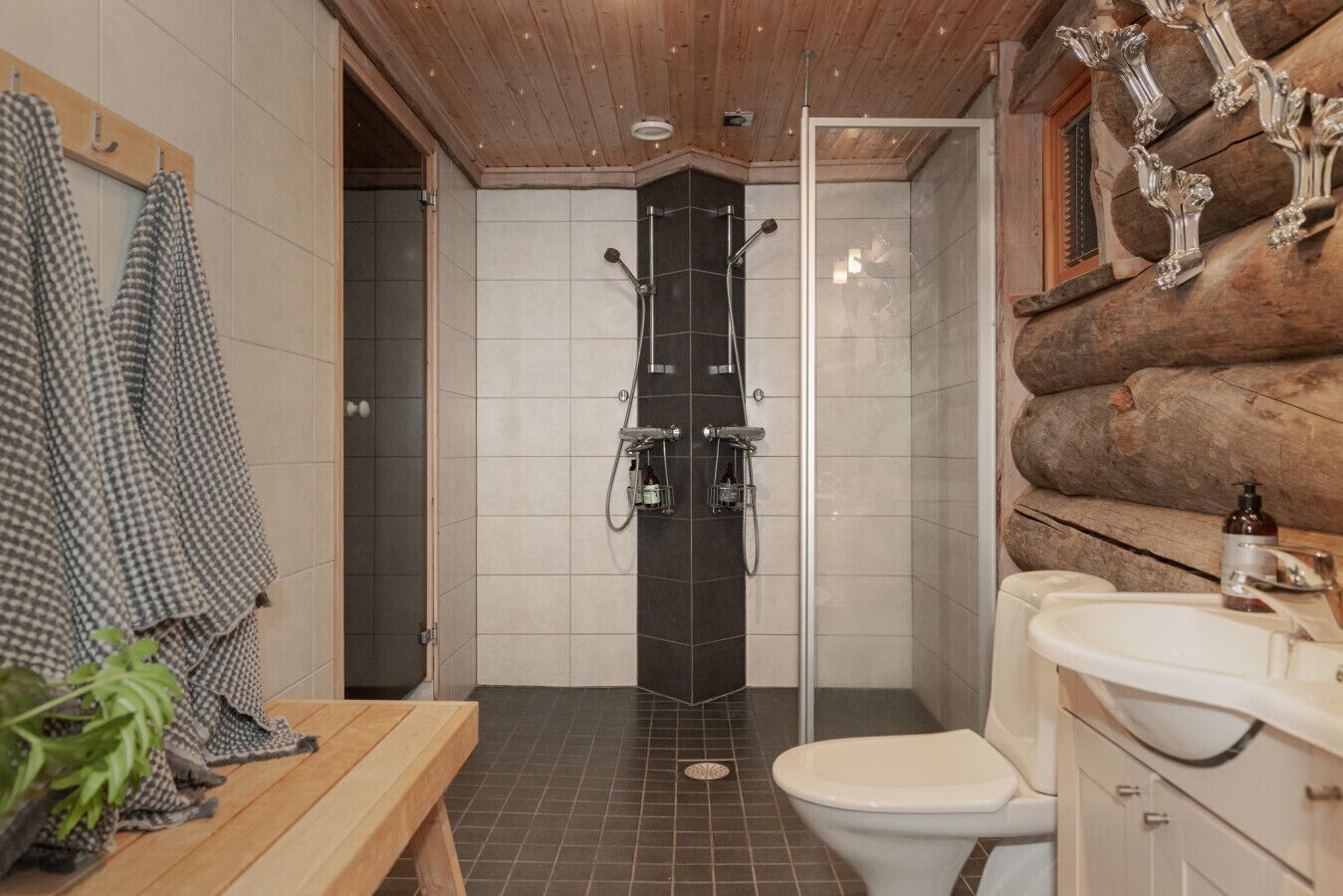 Un baño con ducha, inodoro, lavamanos y techo de madera.