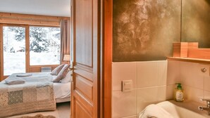 A bedroom with a large window, a bed with a quilt, and a wooden door. - Pistes du Soleil C1 - Four Bedroom Apartment, Sleeps 8 (Le Grand Bornand)