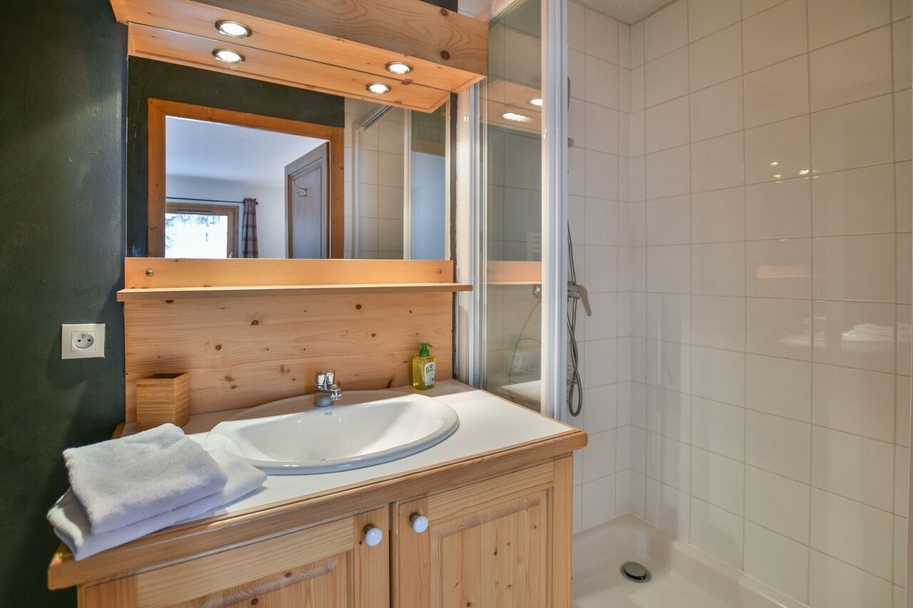 A modern bathroom with a wooden vanity, a large mirror, and a glass shower enclosure.