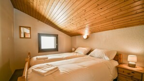 Une chambre avec deux lits, des têtes de lit en bois, une petite fenêtre et une table de chevet avec une lampe.