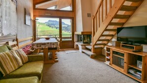 Un salon chaleureux avec un escalier en bois, une télévision et une table entourée de chaises.