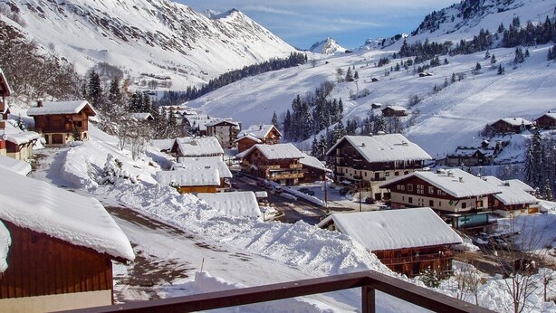 Un village de montagne enneigé, avec des bâtiments en bois et une vue dégagée sur le paysage enneigé environnant.