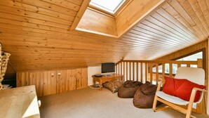 Une pièce mansardée chaleureuse avec des murs en bois et un plafond en pente, équipée d’une télévision, d’un fauteuil à bascule et d’une petite table.