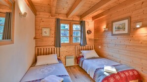 A wooden cabin room with two beds, a window with curtains, and a framed picture on the wall. - Chalet Mitoyen - Solar Est (Le Grand Bornand)