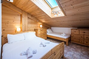 A wooden room with a sloped ceiling, a bed, a bedside table, a nightstand, a dresser, and a skylight.