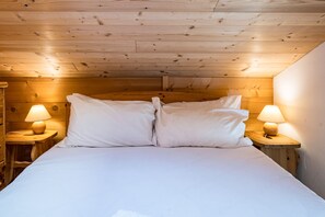 Una habitación con techo de madera, una cama con ropa de cama blanca y dos lámparas de noche.