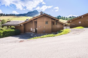 A two-story wooden building with a garage, a sign indicating 'Les P'tits Solaires A', and a mountainous backdrop.