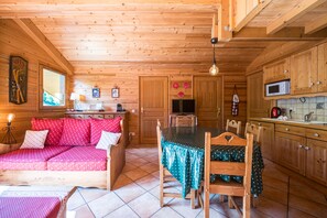 A cozy wooden cabin interior with a sofa, dining table, and kitchen area.