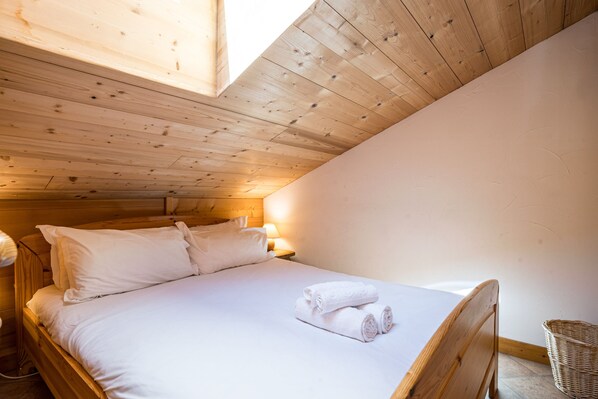 A single bed with white linens, a wooden headboard, and a nightstand with a lamp.