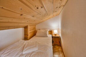 A small, cozy room with a wooden ceiling and walls, a single bed with white bedding, and a nightstand with a lamp. - Pistes du Soleil A15 (Le Grand Bornand)