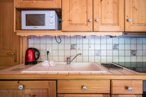 A kitchen with wooden cabinets, a microwave, a kettle, and a sink.