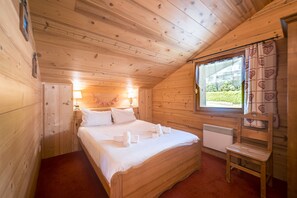 Une chambre dans une cabane en bois, avec un lit simple, des lampes de chevet, une fenêtre avec des rideaux et un radiateur.