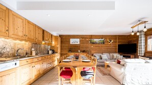 Cozinha moderna com armários de madeira, mesa de jantar e sala de estar com sofá e televisão.