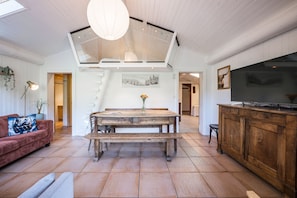 Een ruime woonkamer met een houten eettafel, een rode bank en een televisie op een houten kast.