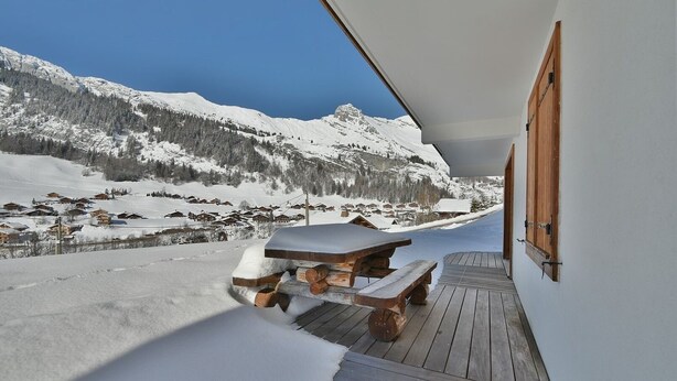 A wooden deck with a picnic table and benches overlooking a snowy mountain village. - Refuge Le Bardeau B2 (Le Grand Bornand)