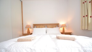 A neatly made bed with white linens and two bedside lamps. - Refuge Le Bardeau B2 (Le Grand Bornand)