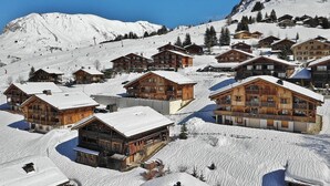 A snow-covered mountain village with wooden chalets, ski slopes, and a clear blue sky. - Refuge Le Bardeau B2 (Le Grand Bornand)
