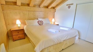 Un dormitorio con techo de madera, una cama con ropa de cama blanca, dos mesitas de noche con lámparas y un armario blanco.