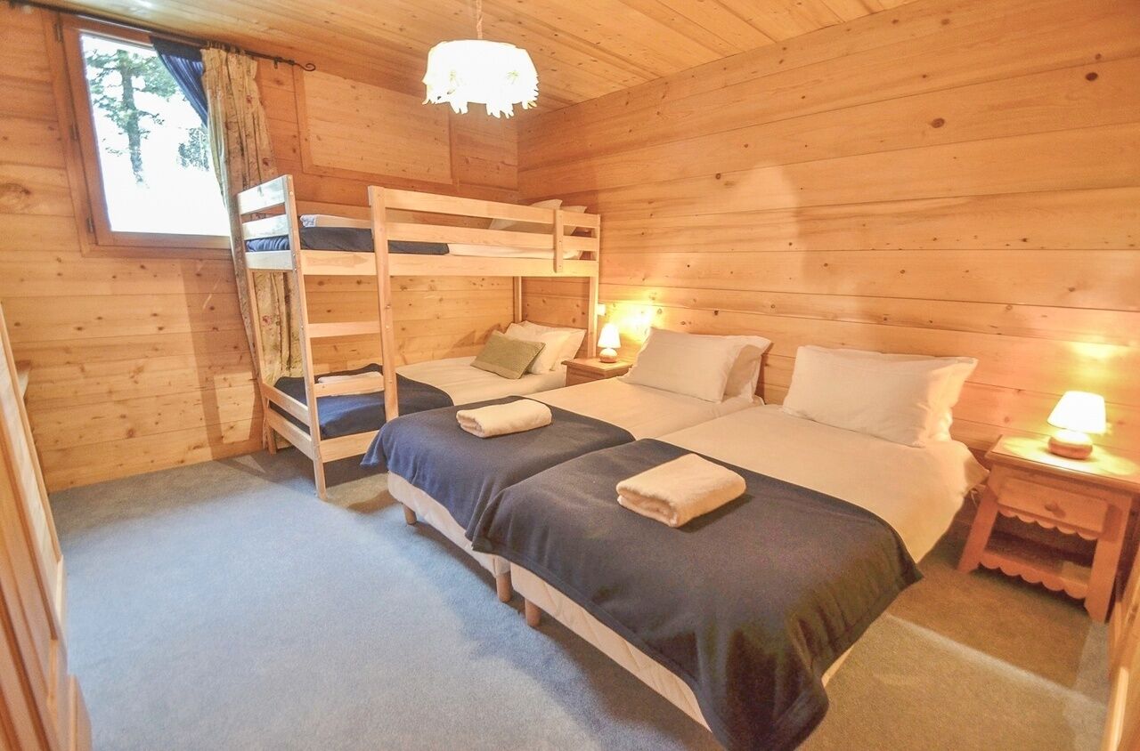 A wooden cabin bedroom with bunk beds, a window with curtains, and a nightstand with a lamp.