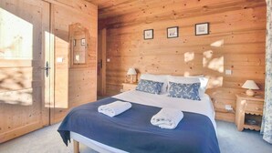 Quarto com painéis de madeira, uma cama, duas mesas de cabeceira e um criado-mudo.