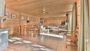 Interior de uma cabana de madeira com área de jantar, sofá e televisão.