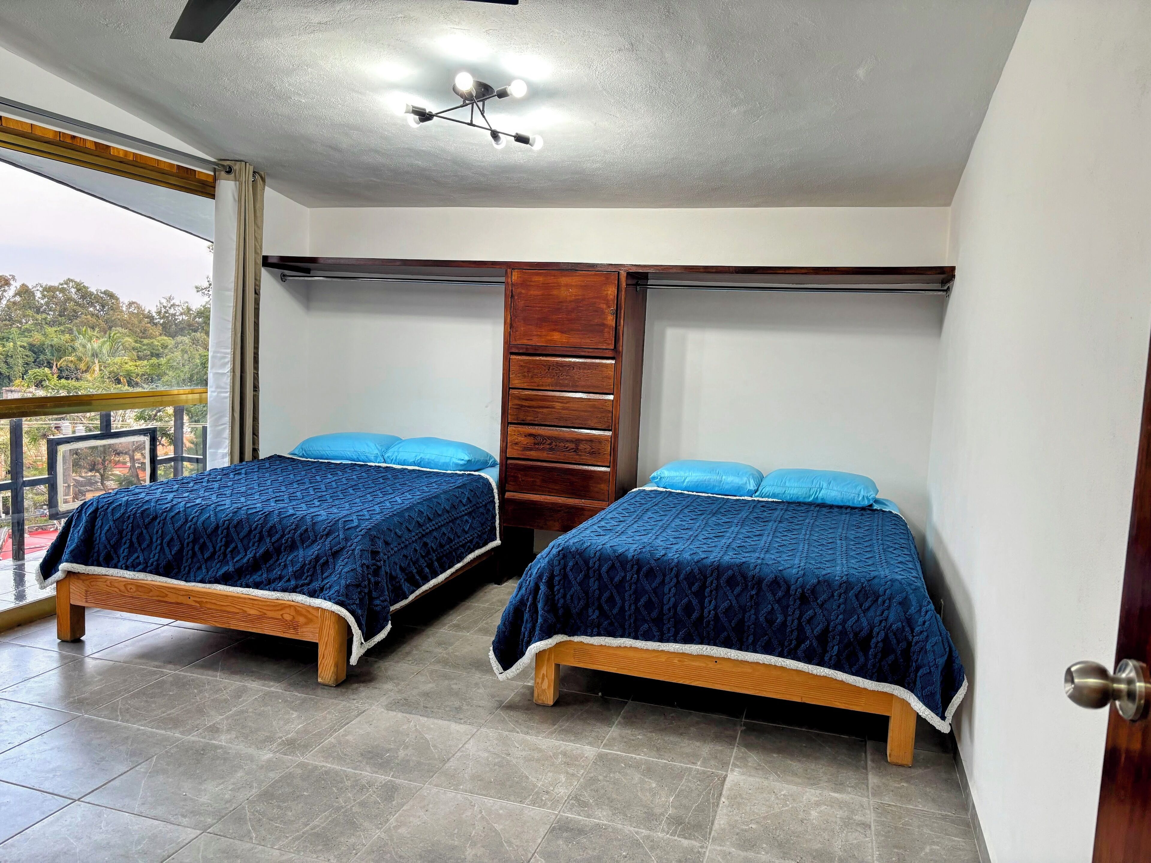 A room with two beds, a wooden wardrobe, and a balcony with a view.