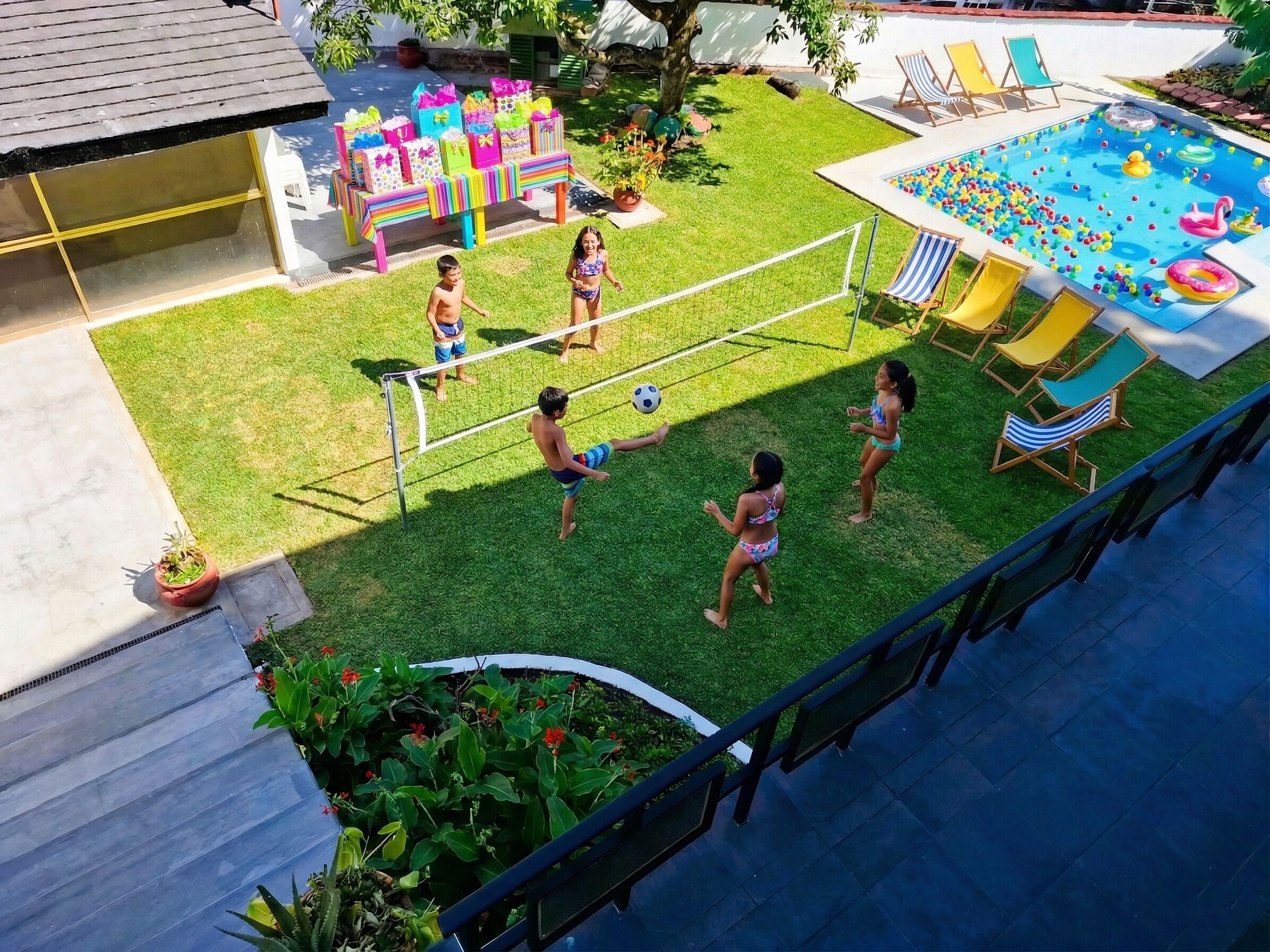 A backyard with a pool, a volleyball net, and a table with gift bags.
